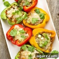 A white serving platter with red, green, and yellow bell pepper halves filled with a Mexican-spiced mix of ground beef, tomatoes, and rice, topped with melted cheese, and garnished with fresh cilantro.