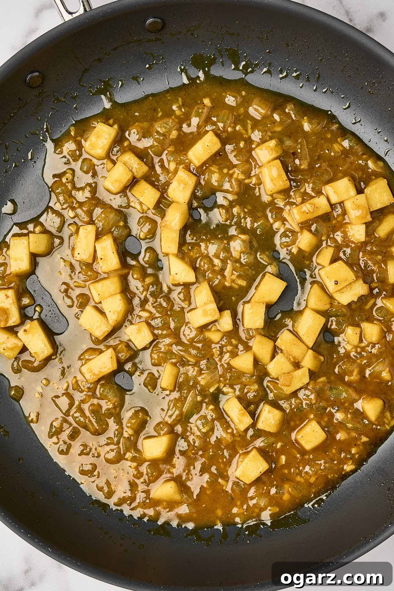 Preparing the creamy curry sauce with sautéed onions, garlic, chunks of apple, and apple cider.