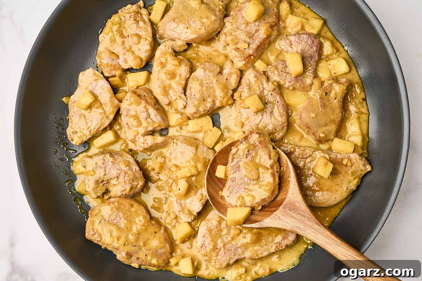 The final step in preparing pork curry with apples, adding the pork medallions back to the pan to finish cooking along with the apples in the creamy curry sauce.