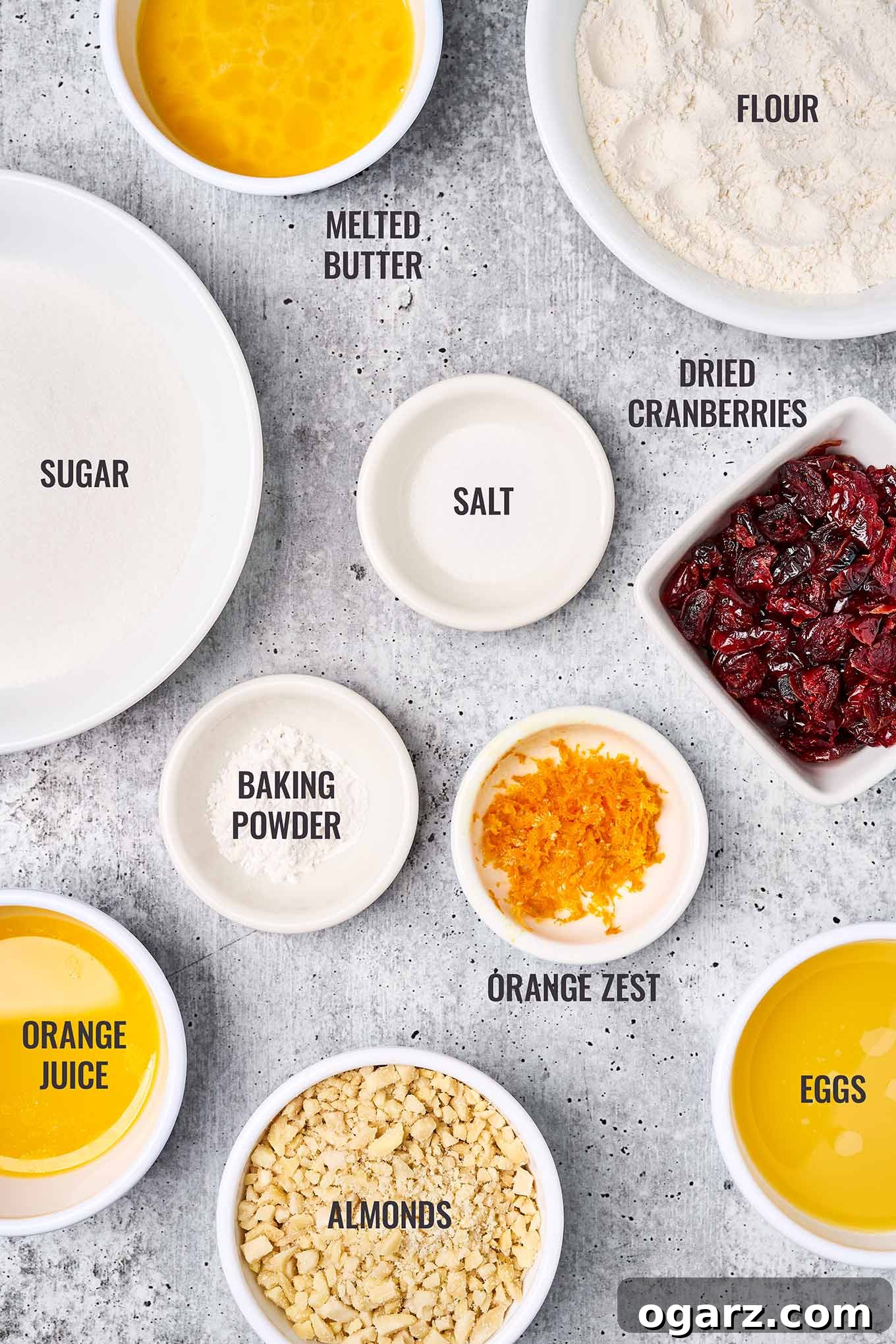Zesty Cranberry Orange Squares 3 A labeled, overhead view of the ingredients for cranberry orange bars including baking ingredients, orange zest, dried cranberries, orange juice, and almonds.