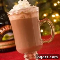 Hot chocolate in a clear Irish coffee mug topped with whipped cream, Christmas lights in the background.