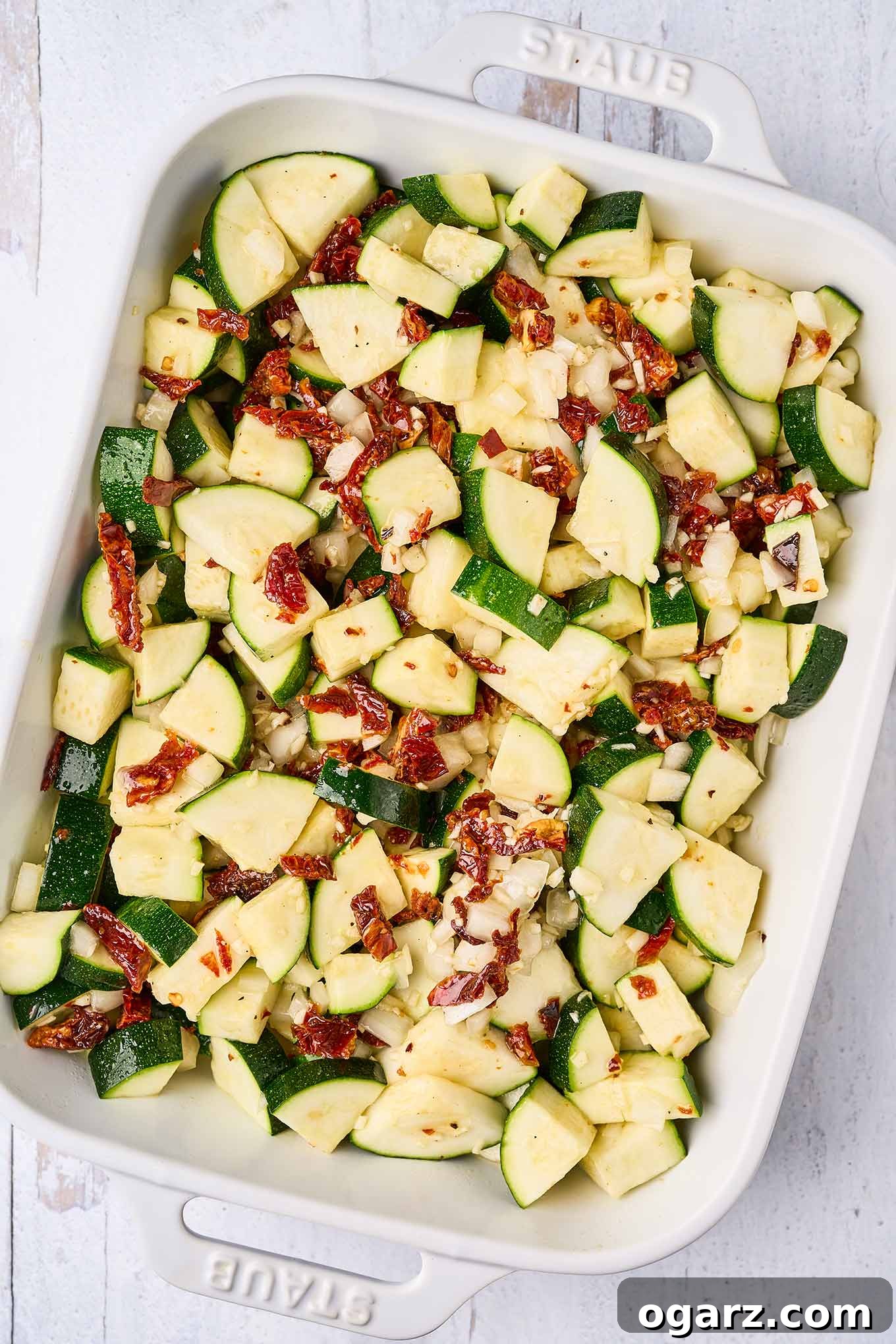 Sun-Kissed Zucchini & Garlic Bake 5 Chunks of zucchini, bits of sun-dried tomatoes, chopped onion, garlic, and olive oil combined in a casserole, ready to be baked.