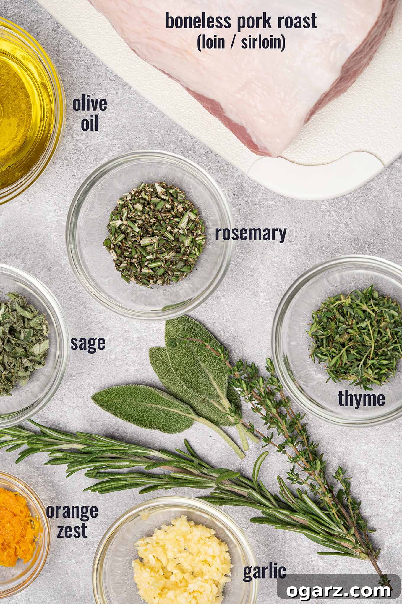 Ingredients for garlic and herb crusted boneless pork roast including fresh sage, rosemary, and thyme, garlic, orange zest, and olive oil.
