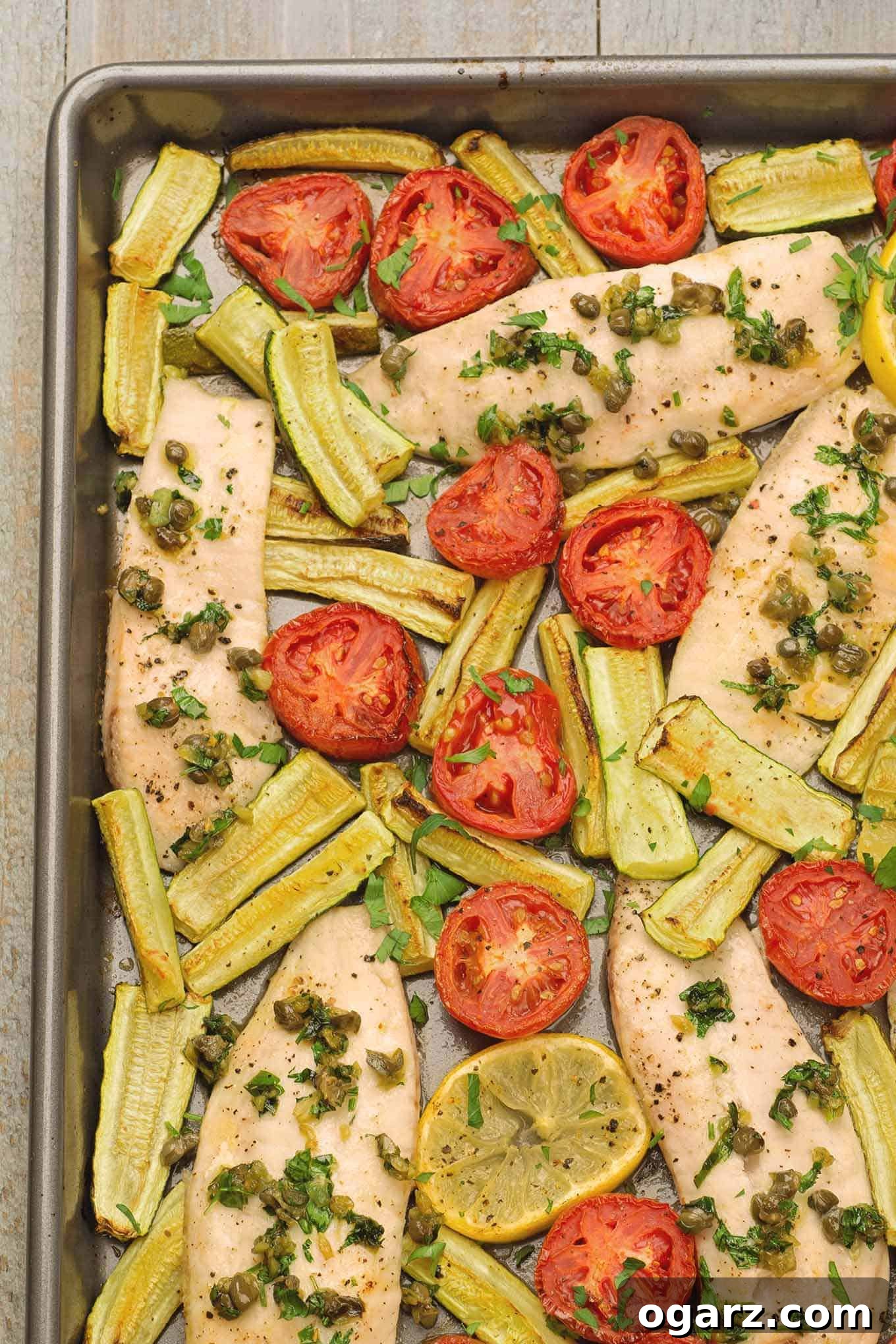 One-Pan Mediterranean Fish Feast 2 An overhead view of a vibrant Mediterranean-style fish dinner on a sheet pan, showcasing golden-brown tilapia fillets, beautifully caramelized plum tomatoes, tender zucchini wedges, bright green capers, and fresh parsley for garnish. This healthy and easy meal is ready to serve.