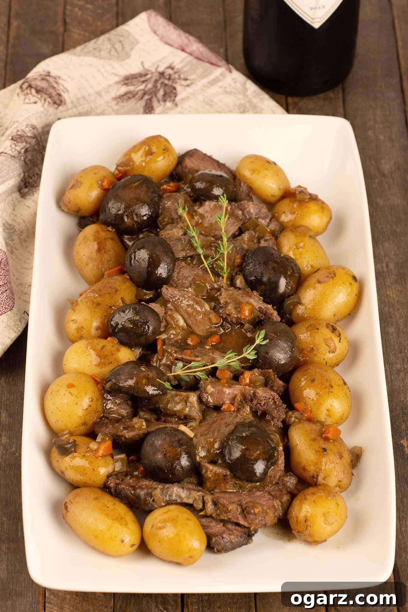 Tender Slow Cooker Pot Roast with Savory Mushrooms 2 A serving platter of sliced slow-cooker pot roast surrounded by braised mushroom caps and baby potatoes, garnished with a sprig of fresh thyme.