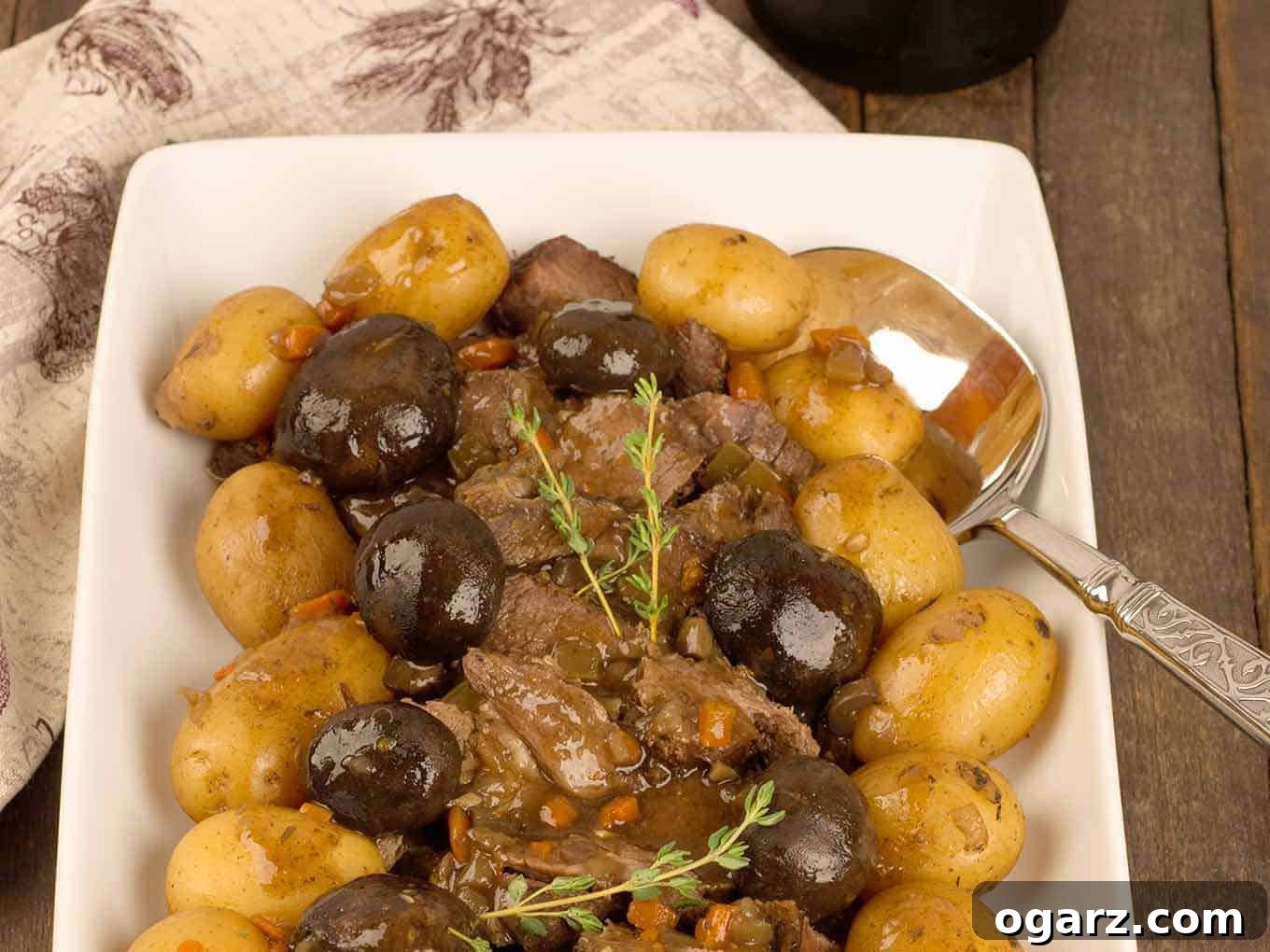 Tender Slow Cooker Pot Roast with Savory Mushrooms 4 A serving platter of sliced slow-cooker pot roast surrounded by braised mushroom caps and baby potatoes, garnished with a sprig of fresh thyme.