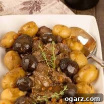 Tender Slow Cooker Pot Roast with Savory Mushrooms 5 A serving platter of sliced slow-cooker pot roast surrounded by braised mushroom caps and baby potatoes, garnished with a sprig of fresh thyme.