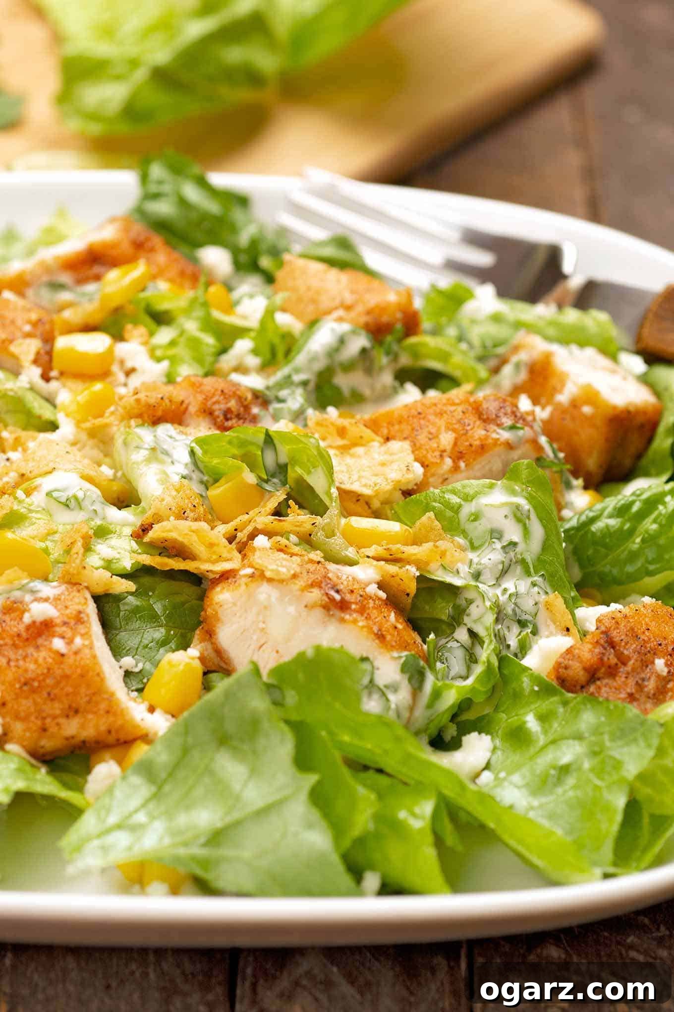 A vibrant serving of Mexican Chicken Caesar Salad, showcasing crispy seasoned chicken, fresh corn, crumbled cotija cheese, and perfectly toasted tortilla chips arranged on a plate.