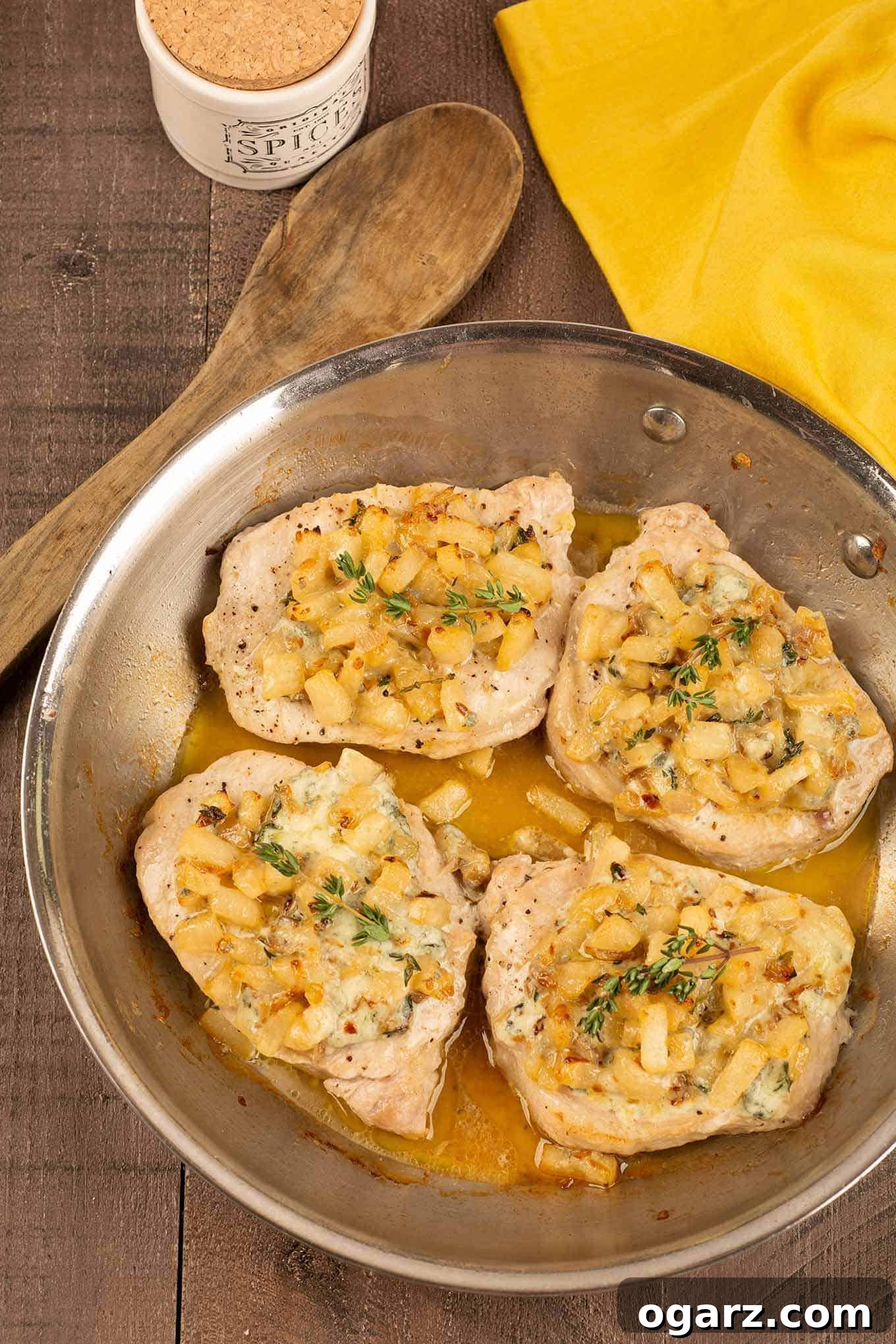 Seared Pork Chops with Caramelized Pears 3 A frying pan with four boneless pork chops in a light pan sauce, topped with pears, blue cheese, and sprigs of thyme.