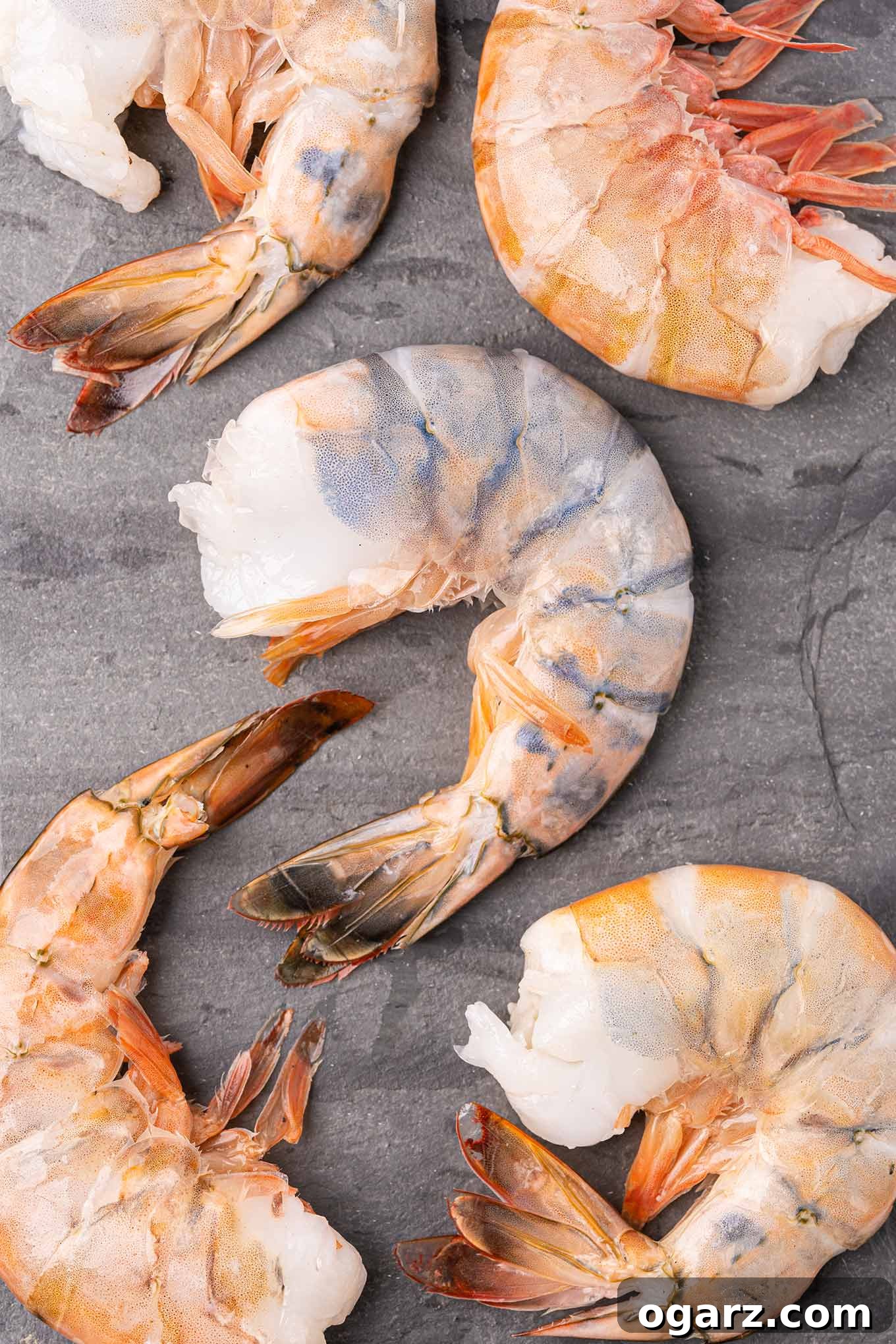 Raw colossal shrimp, expertly peeled and deveined, are artfully arranged on a dark slate board, ready for stuffing and baking.