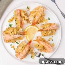 An overhead view of a round white plate filled with baked stuffed colossal shrimp with seafood forks and lemon slices for garnish.