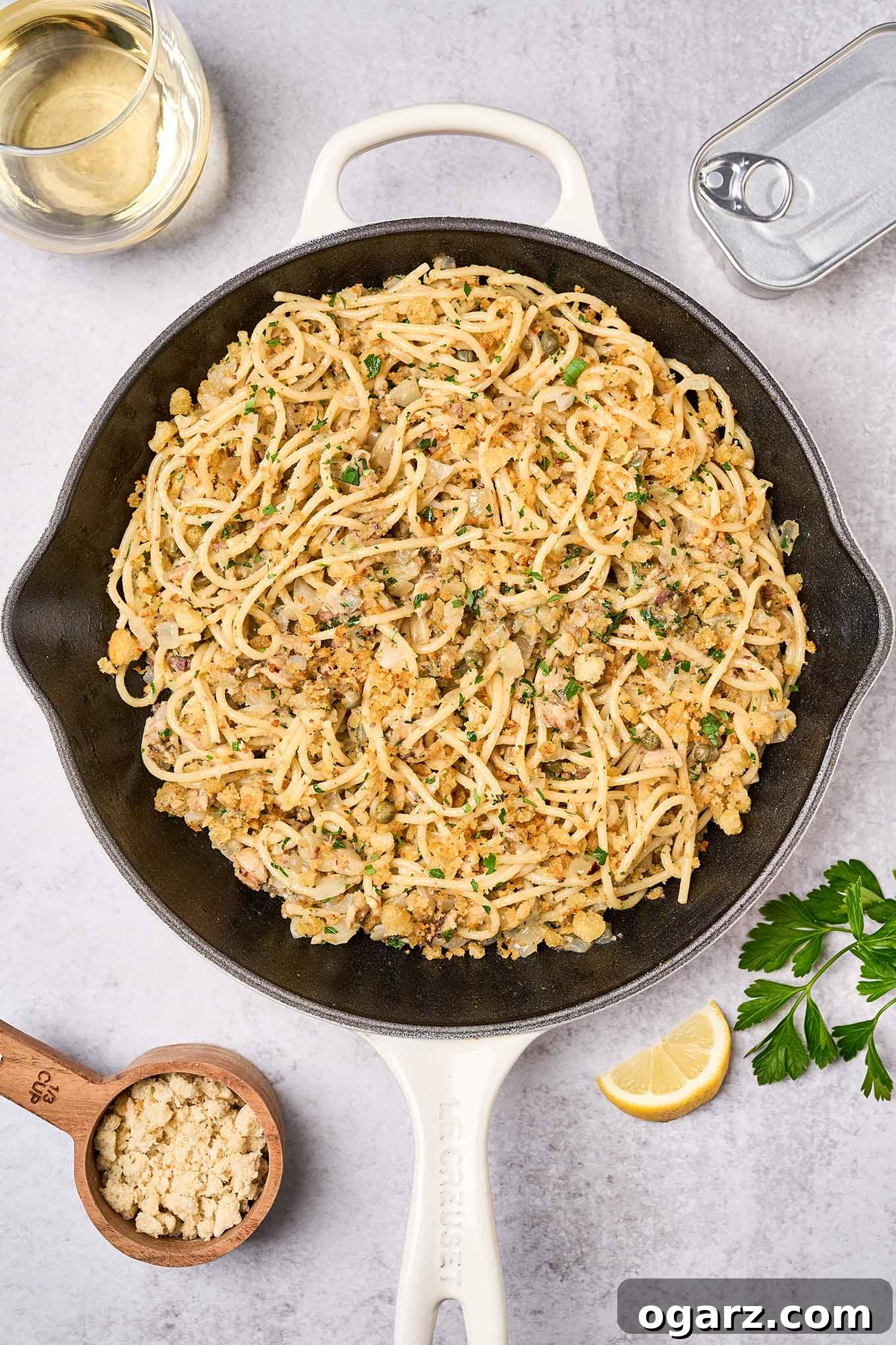 Lemon-Garlic Sardine Pasta with Golden Pangrattato 2 A cast iron pan filled with sardine pasta with a lemon wedge, parsley, tin of sardines, and glass of white wine surrounding it. A vibrant, quick, and healthy meal.