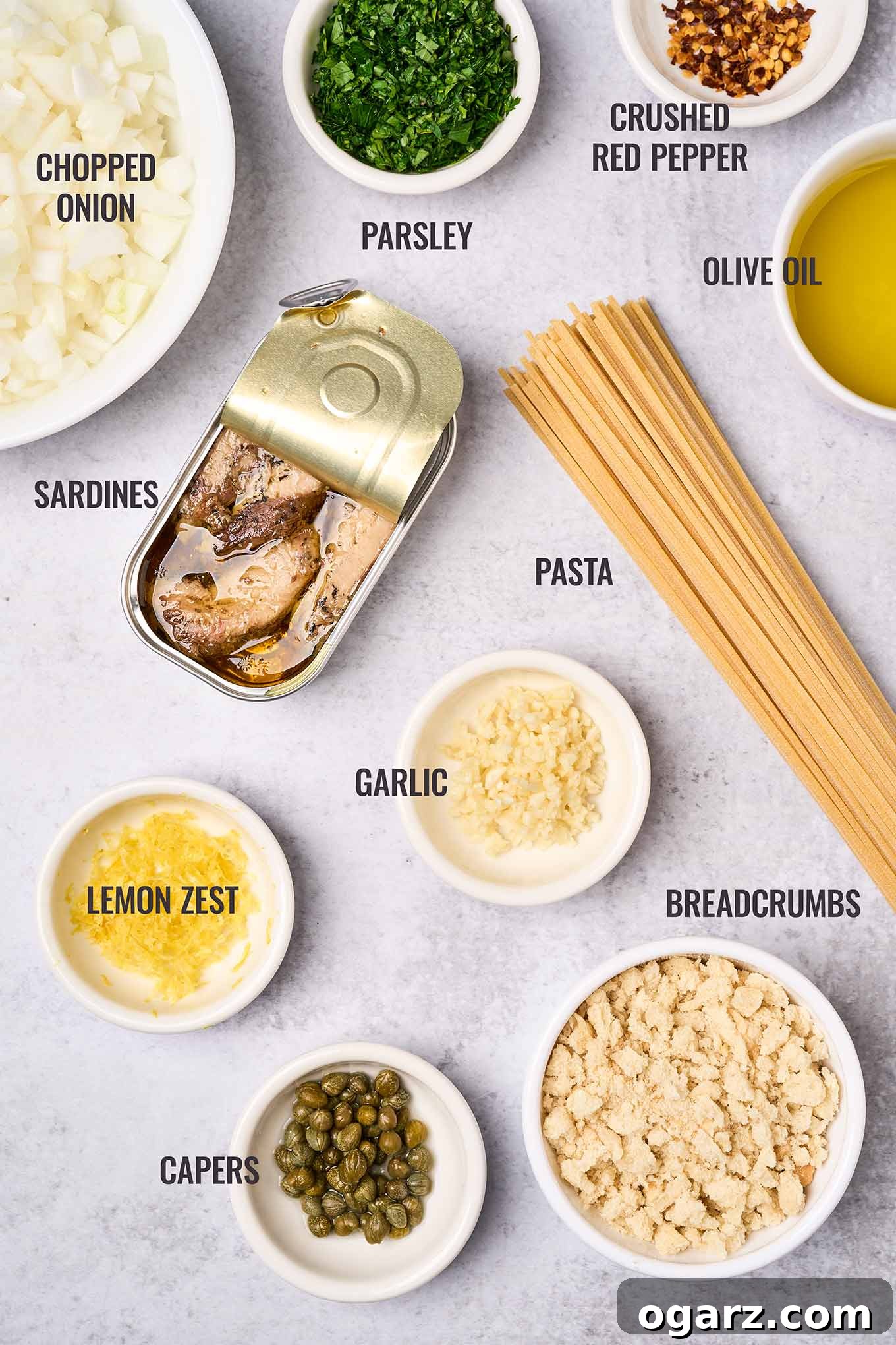 Lemon-Garlic Sardine Pasta with Golden Pangrattato 3 Labeled ingredients for sardine pasta including a tin of sardines, spaghetti, breadcrumbs, capers, lemon zest, garlic, parsley, onion, and crushed red pepper. All fresh and ready to cook.
