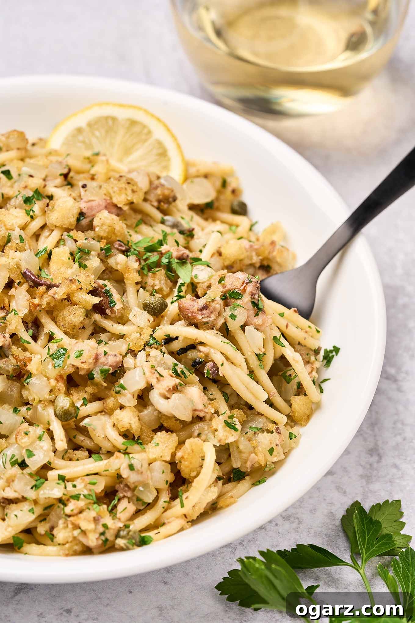 Lemon-Garlic Sardine Pasta with Golden Pangrattato 6 A serving of sardine pasta with toasted breadcrumbs in a bowl with a black fork and a lemon wedge, fresh parsley, and a glass of white wine on the side. Ready to be enjoyed.