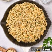 A cast iron pan filled with sardine pasta with a lemon wedge, parsley, tin of sardines, and glass of white wine surrounding it.