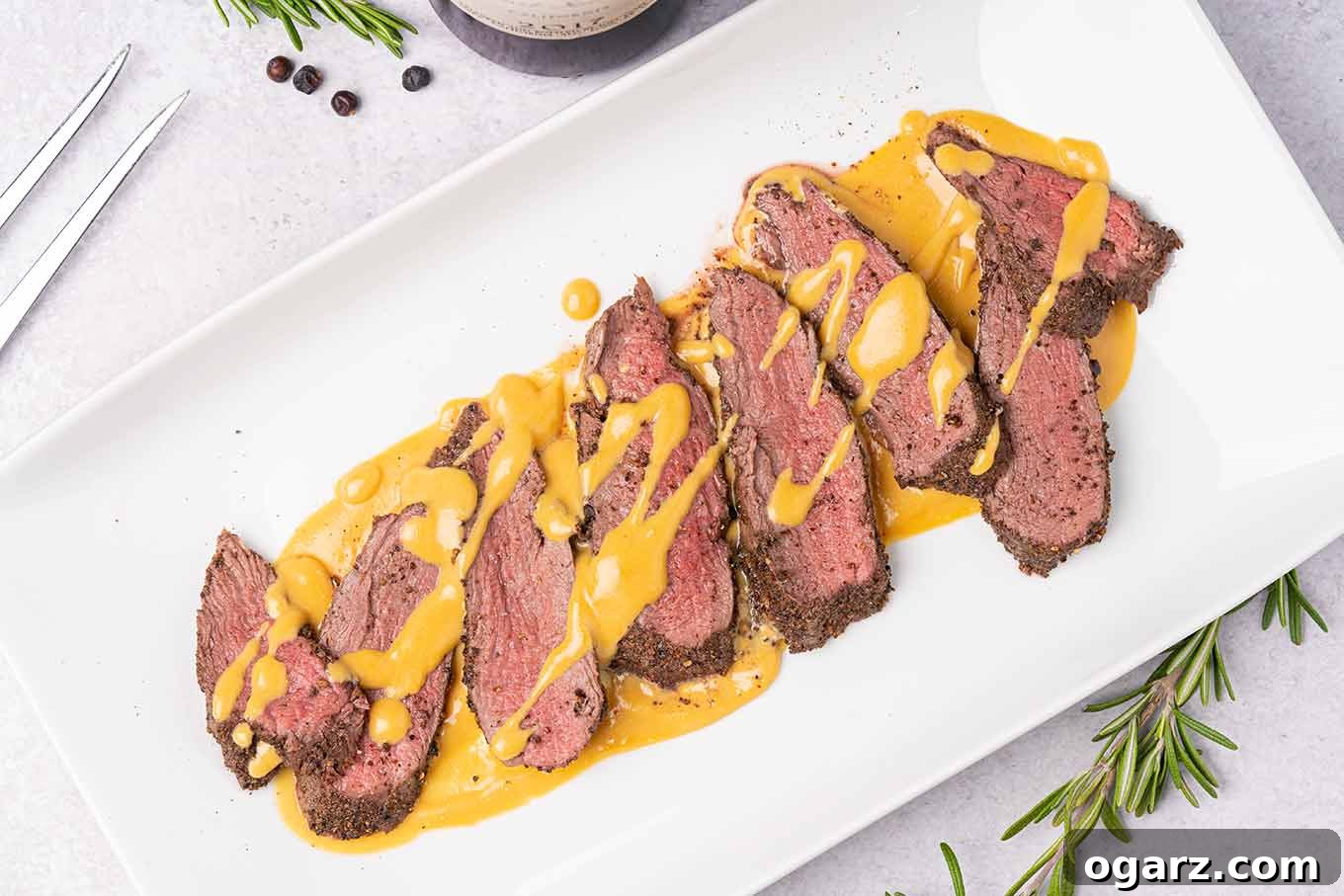 Forest-Kissed Nordic Venison Fillet 4 A white oblong platter arranged with slices of medium-rare roasted venison tenderloin drizzled with gjetost cheese sauce.