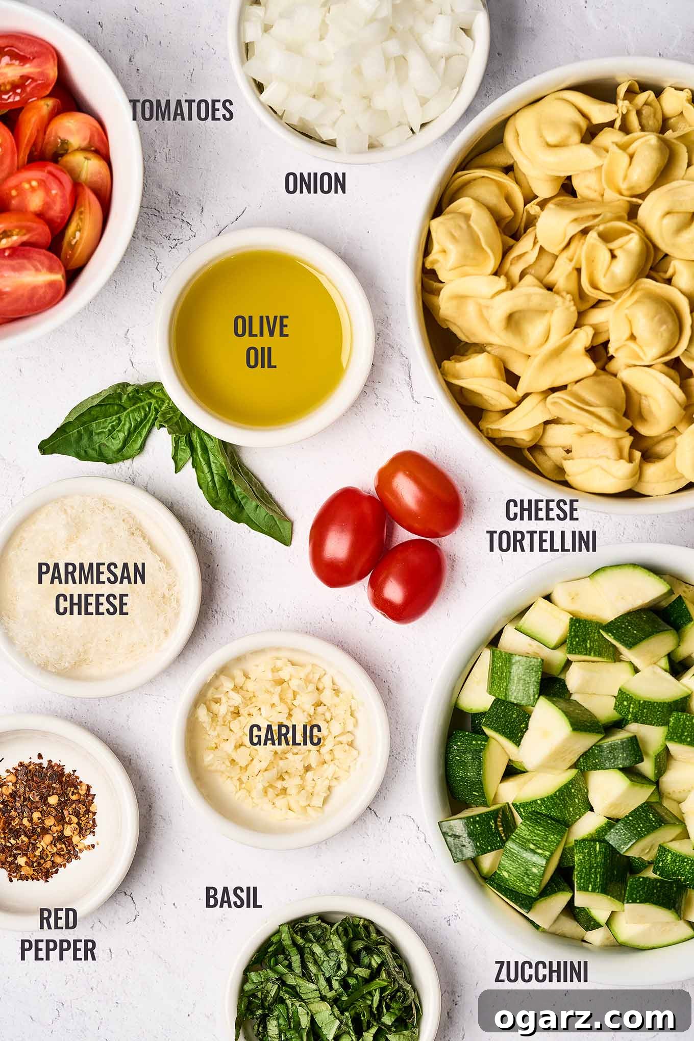 Speedy Cheese Tortellini with Garden Vegetables 3 An organized, overhead display of all the fresh ingredients needed for a delicious cheese tortellini with vegetables: zucchini, fresh cheese tortellini, basil leaves, grape tomatoes, olive oil, onion, garlic, crushed red pepper flakes, and grated Parmesan cheese.