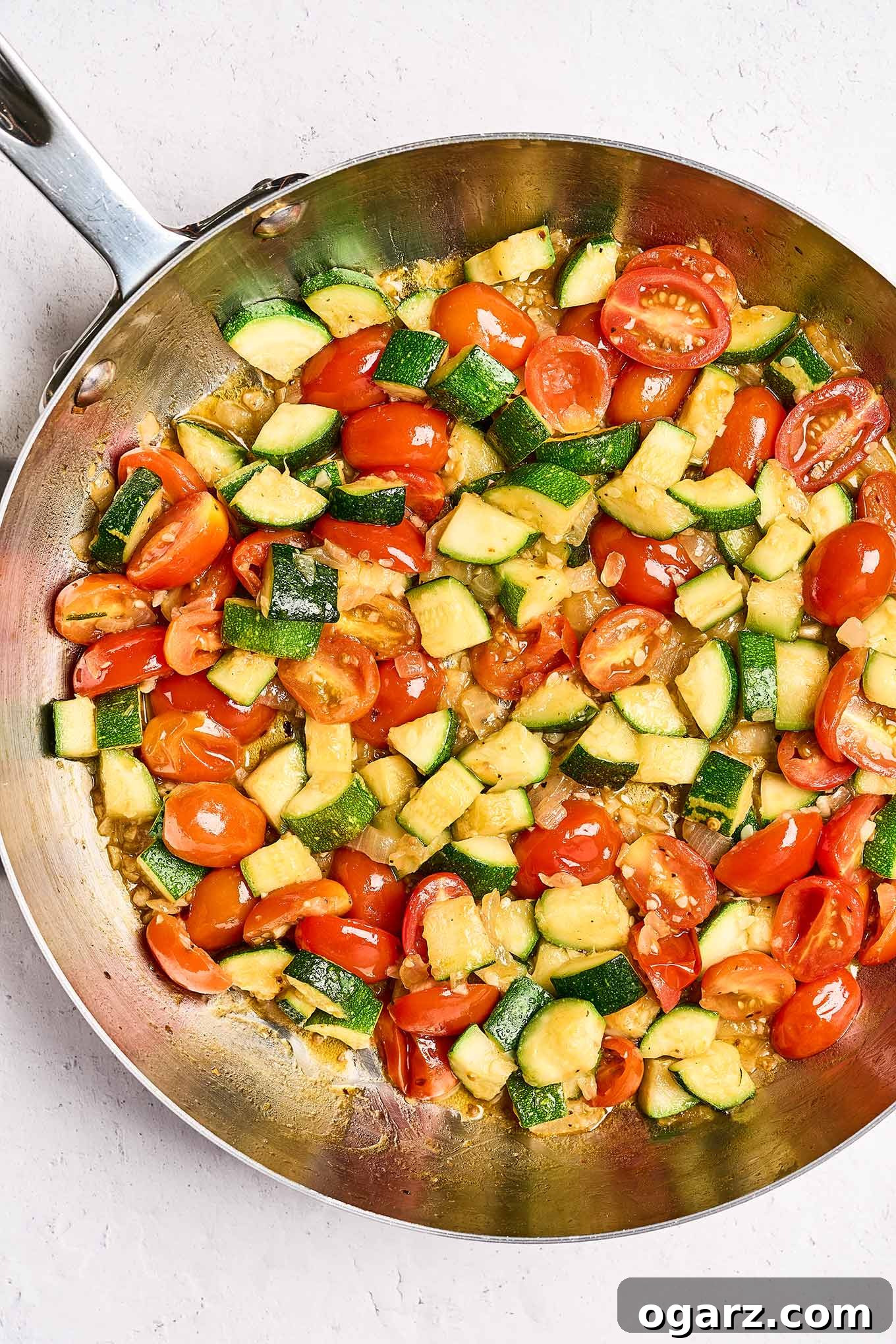Speedy Cheese Tortellini with Garden Vegetables 5 A frying pan showcasing a vibrant mix of sautéed onion, garlic, tender zucchini chunks, and perfectly halved grape tomatoes, awaiting combination with cooked cheese tortellini.