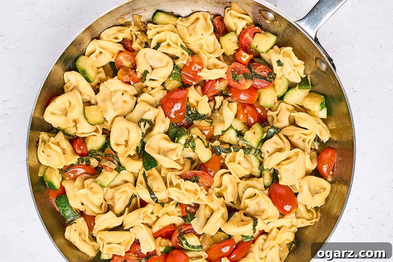 Speedy Cheese Tortellini with Garden Vegetables 6 A frying pan presenting a harmonious blend of freshly cooked cheese tortellini, tender sautéed zucchini, gently wilted grape tomatoes, and fragrant fresh basil, ready for plating and serving.