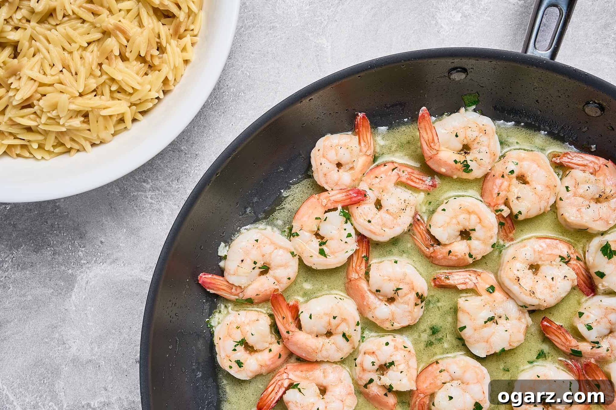 Shrimp scampi simmering in garlic butter sauce, next to a bowl of cooked orzo ready for plating.