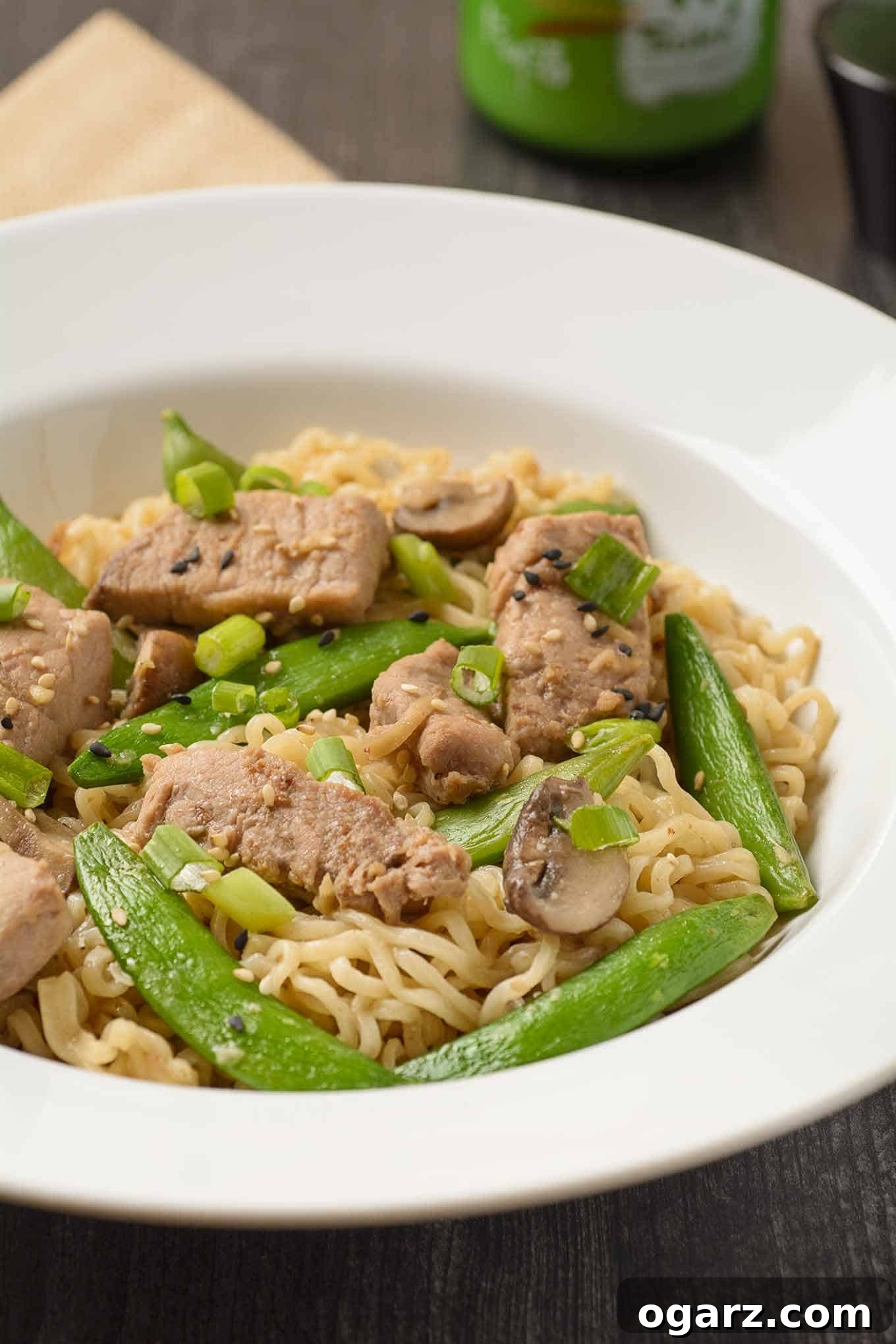 Pork Ramen Skillet Sensation 3 A shallow bowl of ramen noodles tossed with stir-fried pork, sugar snap peas, and scallions with a bottle of sake in the background.