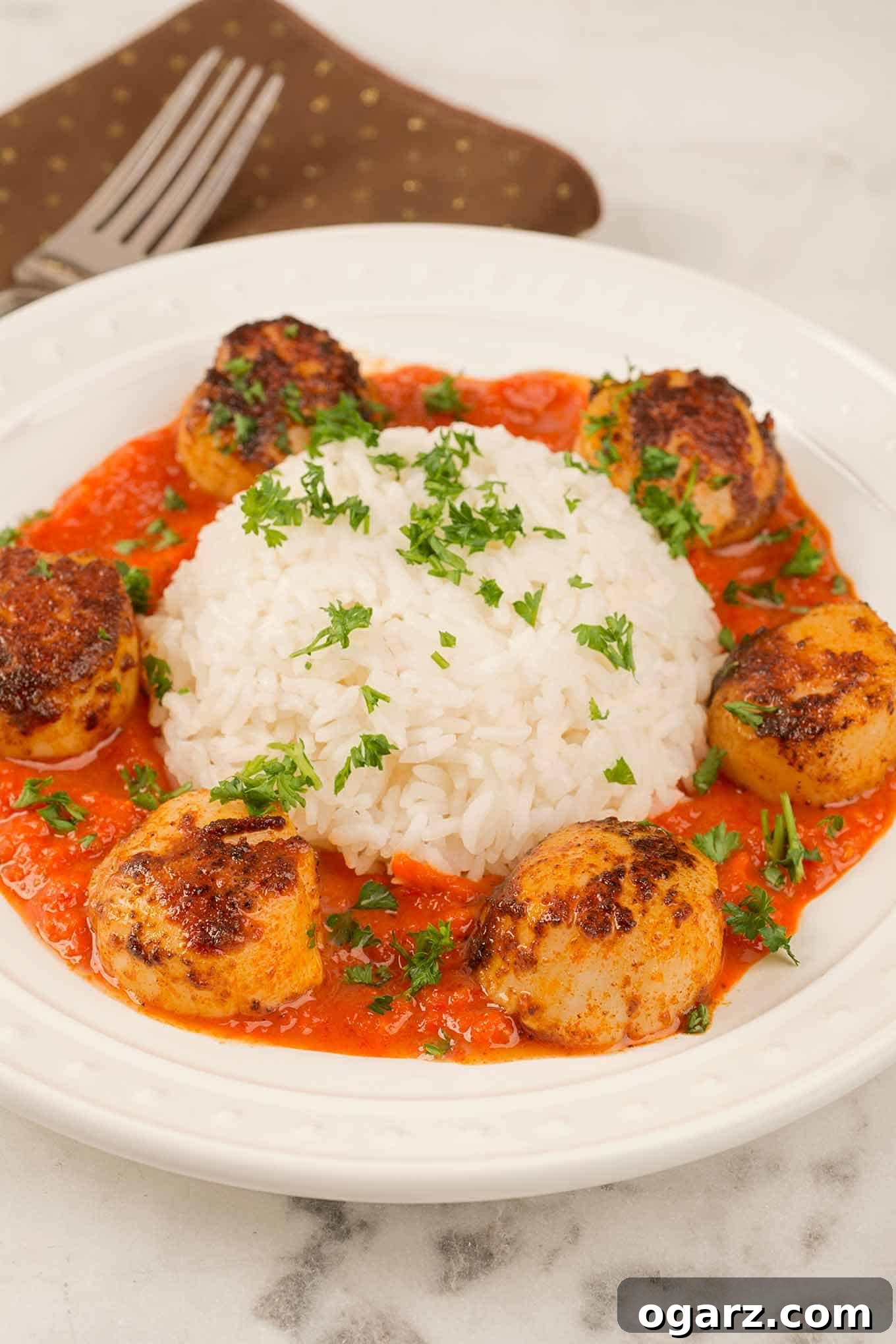 Seared Scallops with Vibrant Red Pepper Reduction 2 A plate of paprika-crusted, pan-seared sea scallops in roasted red pepper sauce arranged around a serving of white rice, all garnished with chopped parsley.