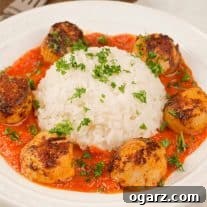 Seared Scallops with Vibrant Red Pepper Reduction 4 A plate of paprika-crusted, pan-seared sea scallops in roasted red pepper sauce arranged around a serving of white rice, all garnished with chopped parsley.