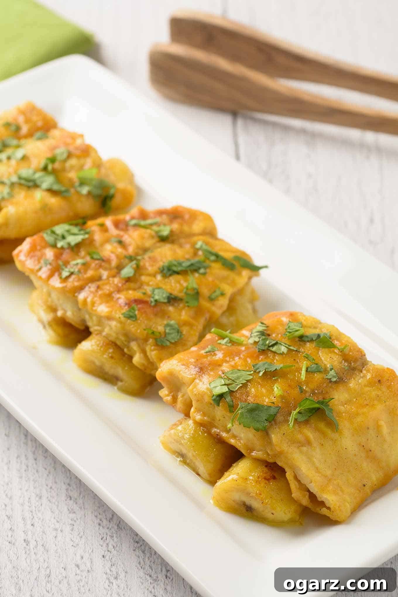 An oblong serving plate with three pieces of pan-fried fish fillets served over bananas sautéed in a light curry sauce. A vibrant, flavorful dish for a quick meal.