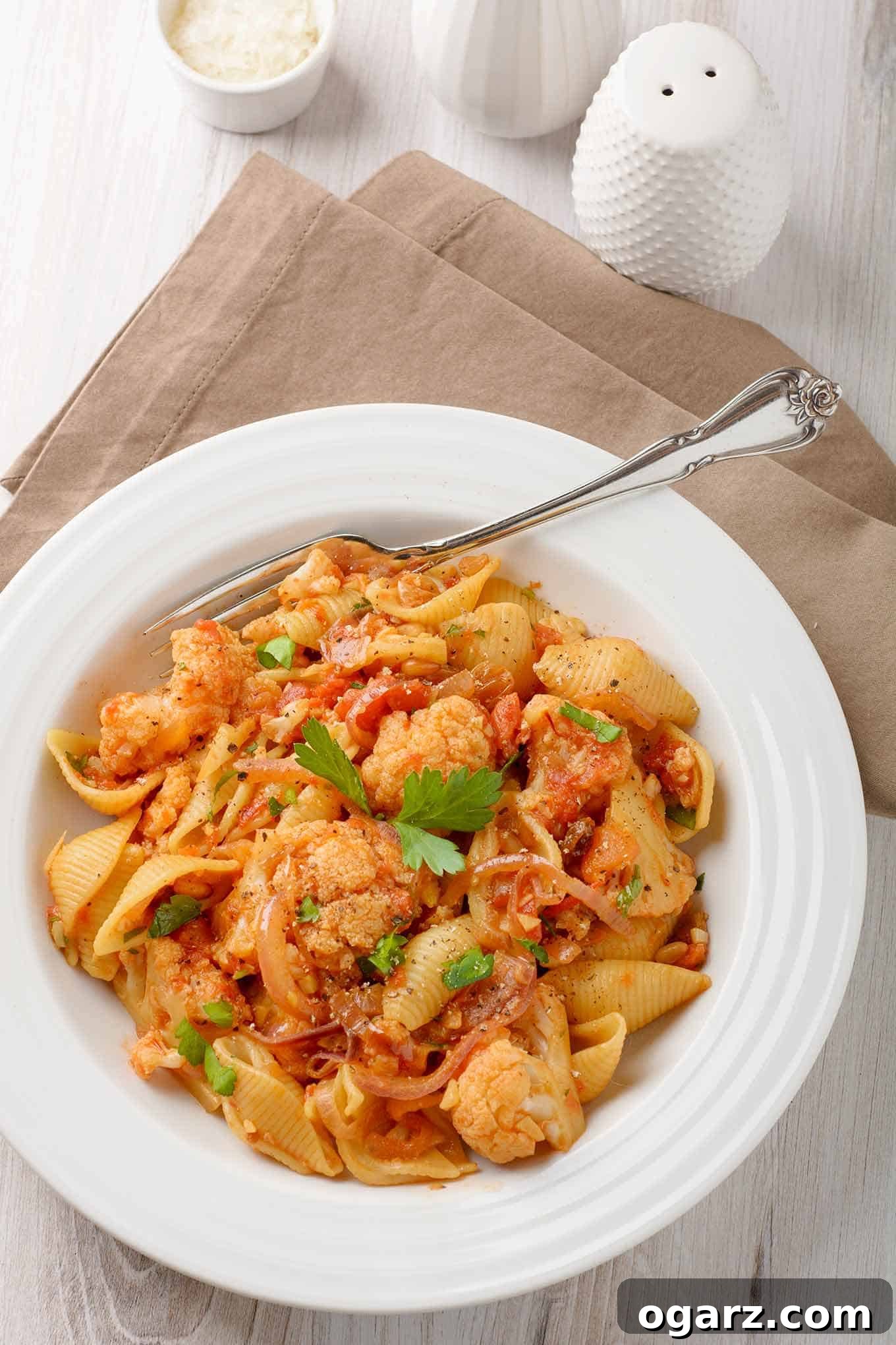 Rustic Sicilian Cauliflower Pasta 2 A vibrant bowl of Sicilian pasta with perfectly cooked shell pasta, tender steamed cauliflower florets, golden raisins, toasted pine nuts, and a rich tomato-based sauce infused with anchovies and saffron. This visually appealing dish showcases a unique blend of sweet, savory, and umami flavors.
