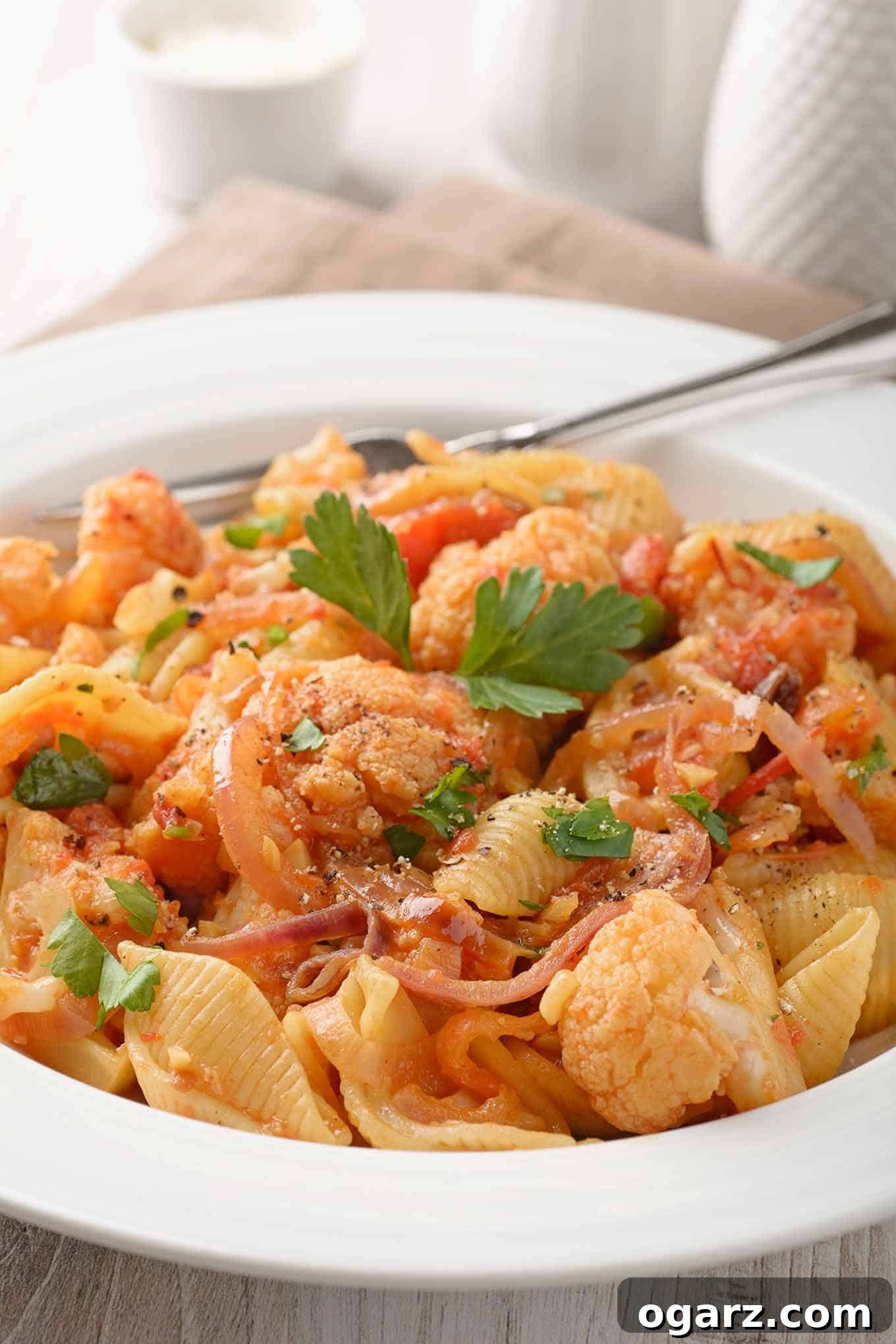 Rustic Sicilian Cauliflower Pasta 3 A tantalizing close-up of Sicilian pasta with cauliflower, featuring perfectly cooked shell pasta, vibrant cauliflower florets, diced tomatoes, thinly sliced red onion, golden raisins, toasted pine nuts, and hints of savory anchovies. This image highlights the rich textures and diverse ingredients of this traditional meatless dish.