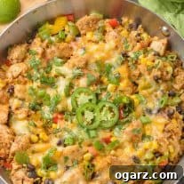 A frying pan filled with Southwest-style chicken and cauliflower rice with bell peppers, corn, scallions, beans, garnished with sliced jalapenos and cilantro.