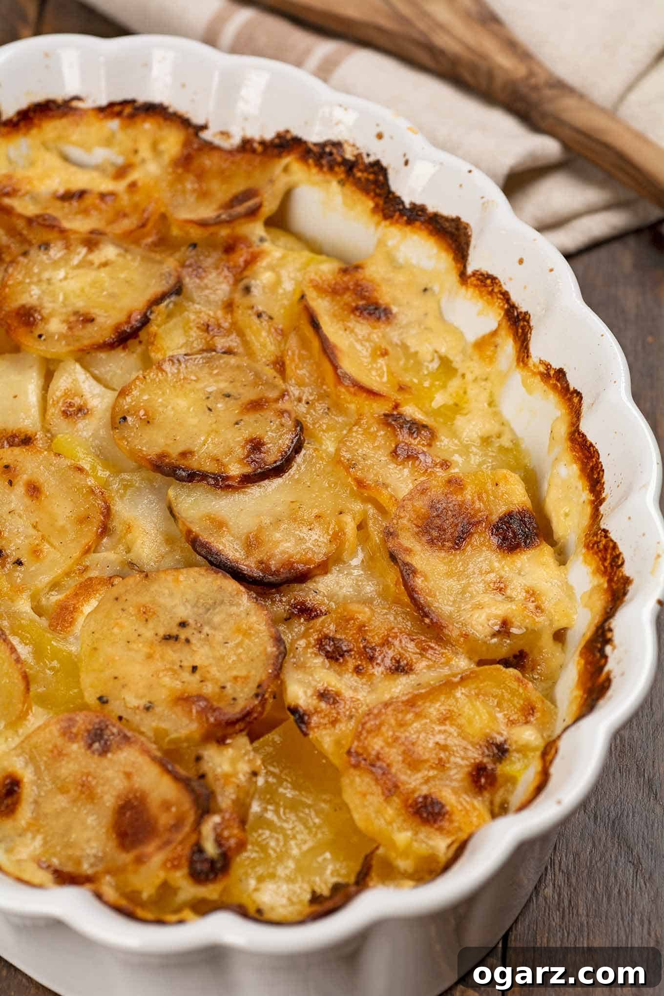 Creamy Potato Gratin 3 A close-up view of a baked oval casserole of scalloped potatoes, revealing distinct, creamy layers and a golden-brown top, with a portion already served.