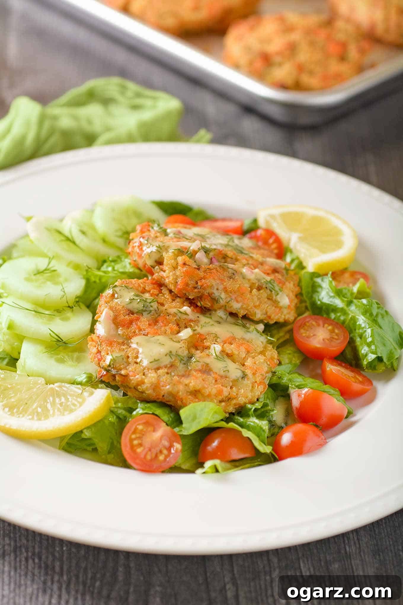 Crispy Salmon Quinoa Fritters 3 Baked salmon quinoa cakes served with a fresh salad and lemon-dill dressing, with more patties on a baking sheet in the background.