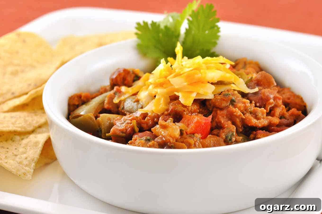 Robust Turkey Sausage Chili 2 A vibrant bowl of Turkey Sausage Chili garnished with fresh cilantro and shredded cheese, served with tortilla chips on the side.