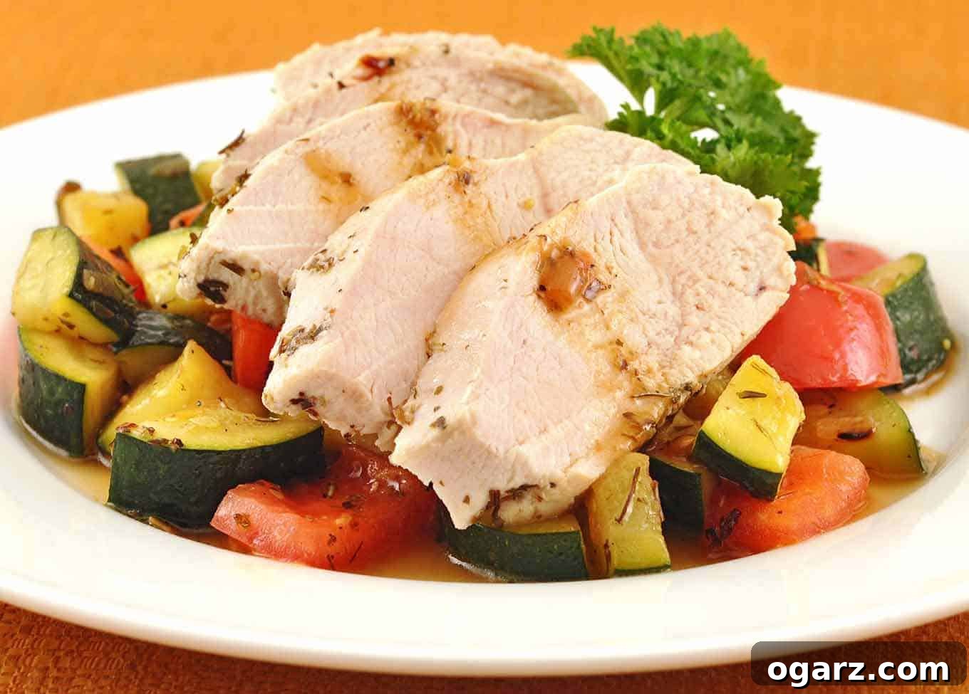 Velvety Butter Poached Chicken with Garden Vegetables 2 Sliced herb and butter poached chicken breast served over a medley of sautéed zucchini and red bell peppers, garnished with parsley on a white plate.
