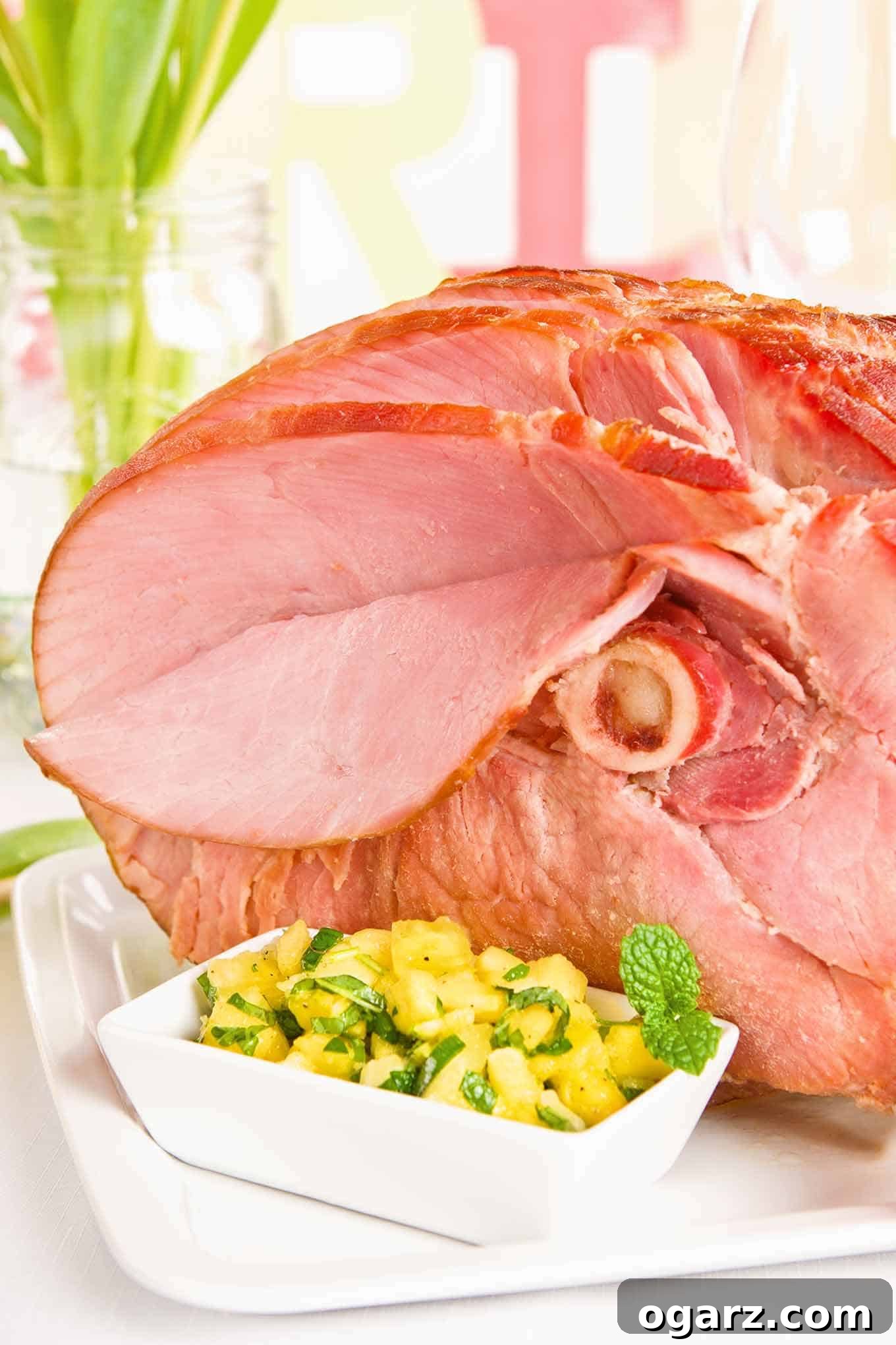 A beautifully spiral-sliced, honey-glazed baked ham on a serving platter, accompanied by a vibrant bowl of fresh pineapple mint chutney. The table is adorned with spring-inspired decor, creating an inviting festive atmosphere.