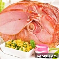 A spiral-sliced, glazed, baked ham on a serving platter with an accompanying bowl of pineapple mint chutney, surrounded by spring table decor.