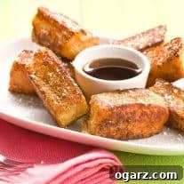 A serving of French toast sticks made with Hawaiian rolls, dusted with powdered sugar, and served with a small bowl of maple syrup for dipping.
