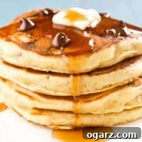 Decadent Chocolate Chip Pancakes with Crispy Candied Bacon 4 A stack of four chocolate chip pancakes topped with a few extra chocolate chips, a pat of butter, and a drizzle of maple syrup.