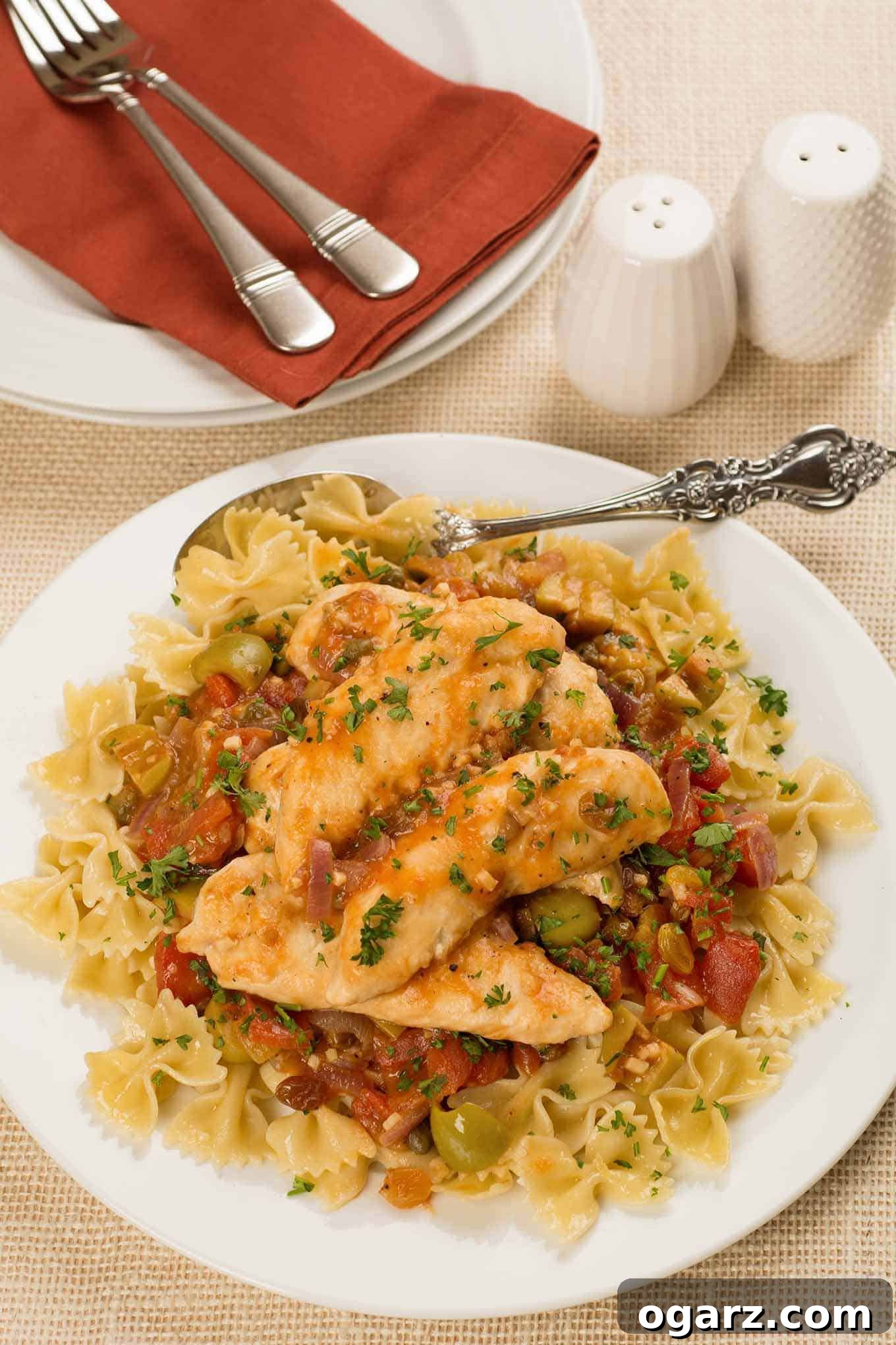 Sun-Drenched Sweet and Sour Chicken 2 A serving plate of farfalle pasta topped with pan-seared chicken tenderloins simmered in a tangy sauce of diced tomatoes, green olives, capers and golden raisins.