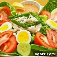A serving of crab Louie salad, lettuce, tomatoes, hard cooked eggs, crab, cucumber, asparagus, dressing, and a lemon wedge