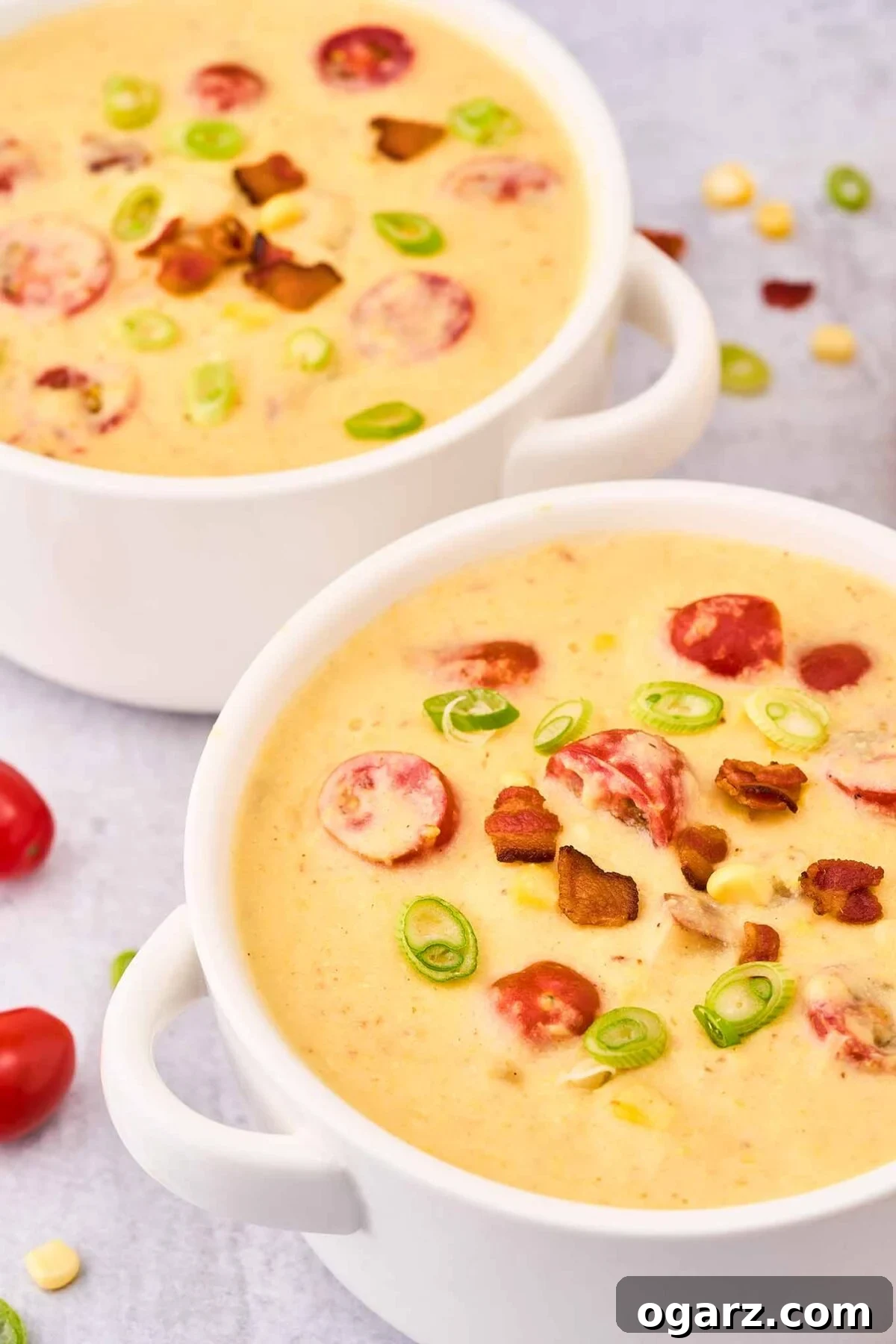 Smoky Bacon & Tomato Corn Chowder 9 A single white serving bowl filled with creamy corn chowder, beautifully garnished with crispy bacon and fresh tomatoes, positioned in the foreground. A second, subtly blurred bowl of chowder rests in the background, creating an appealing depth of field.