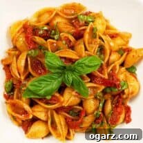 Serving dish filled with shell pasta tossed with sun-dried tomatoes, balsamic glaze, and fresh basil.