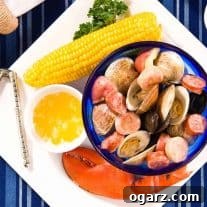 Plate containing lobster claw, ear of corn, bowl of melted butter, nutcracker, and bowl of steamed clams, mussels, sausage, and potatoes.