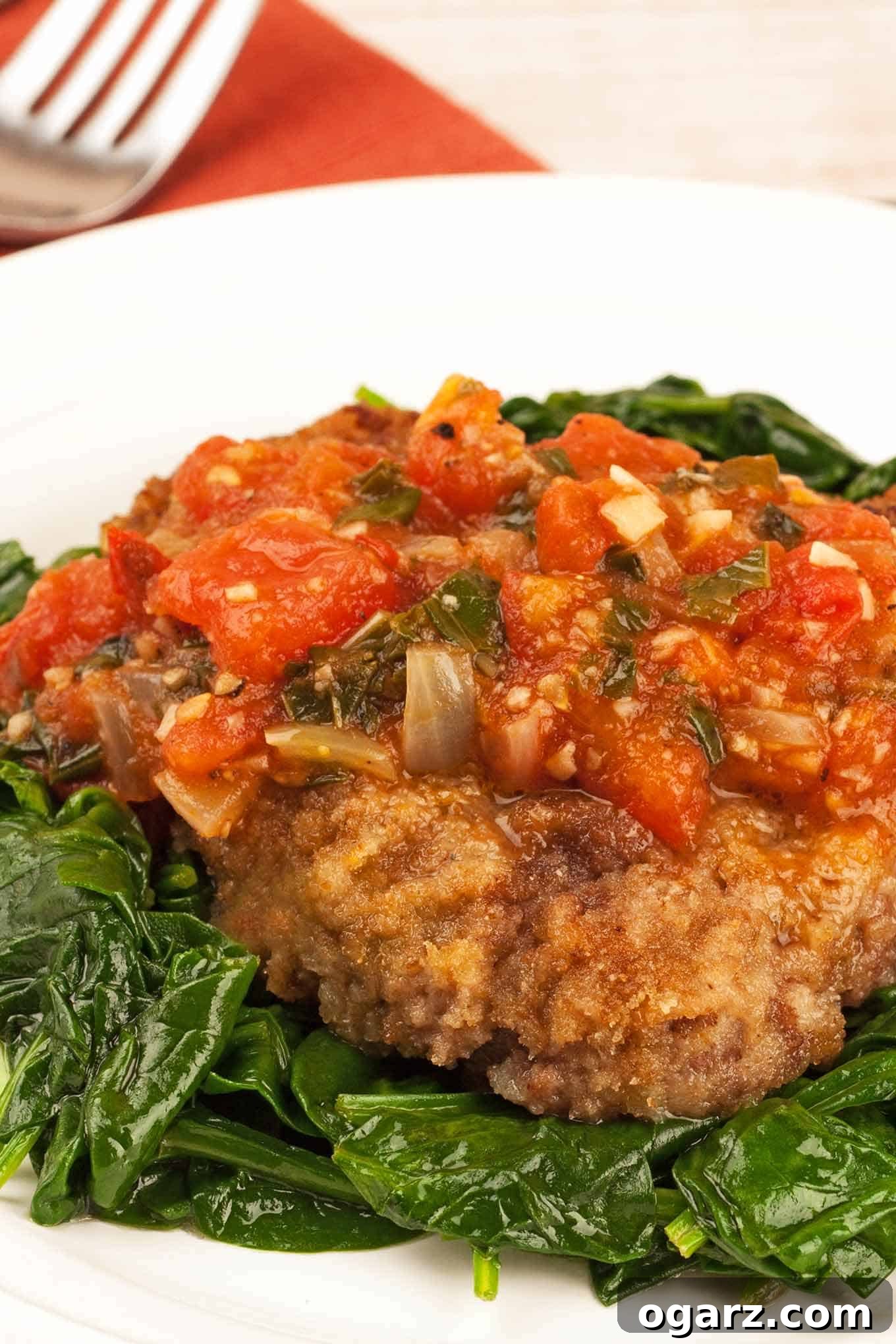 Milanese Steak Perfection 2 A vibrant plate featuring golden-brown steak alla Milanese, generously topped with a rich tomato and herb marinara sauce, served on a bed of fresh sautéed spinach on a pristine white plate.