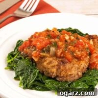 Milanese Steak Perfection 4 A plate of lightly breaded steak alla Milanese topped with tomato sauce, served over a bed of sautéed spinach.