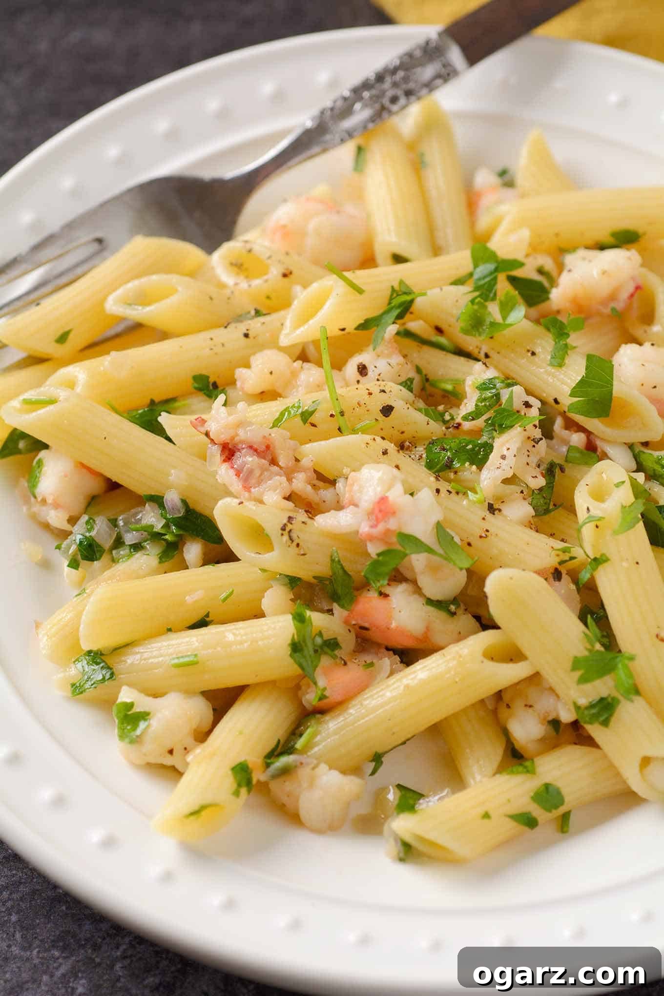 Decadent Lobster Truffle Pasta 3 A closeup view of penne pasta in a creamy white wine butter sauce, featuring juicy chunks of lobster, finely chopped shallot, and fresh parsley, all glistening with truffle oil.