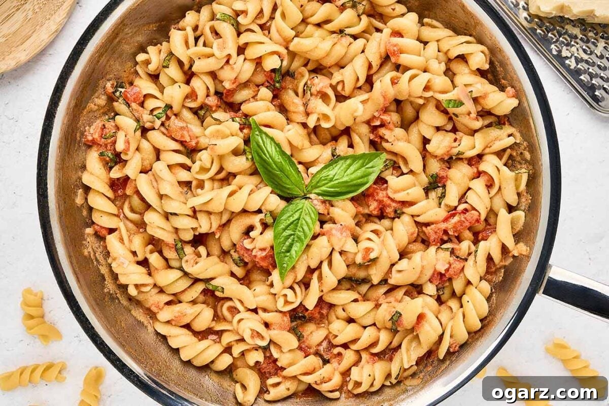 A pan filled with pasta in creamy mascarpone tomato sauce with fresh basil, ready to be plated and served.