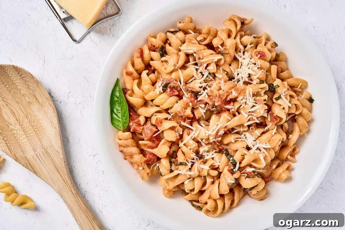 A bowl of rotini tossed with a creamy tomato sauce made with mascarpone cheese, a wooden spoon and a cheese grater in the background.