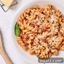A bowl of rotini tossed with a creamy tomato sauce made with mascarpone cheese, a wooden spoon and a cheese grater in the background.